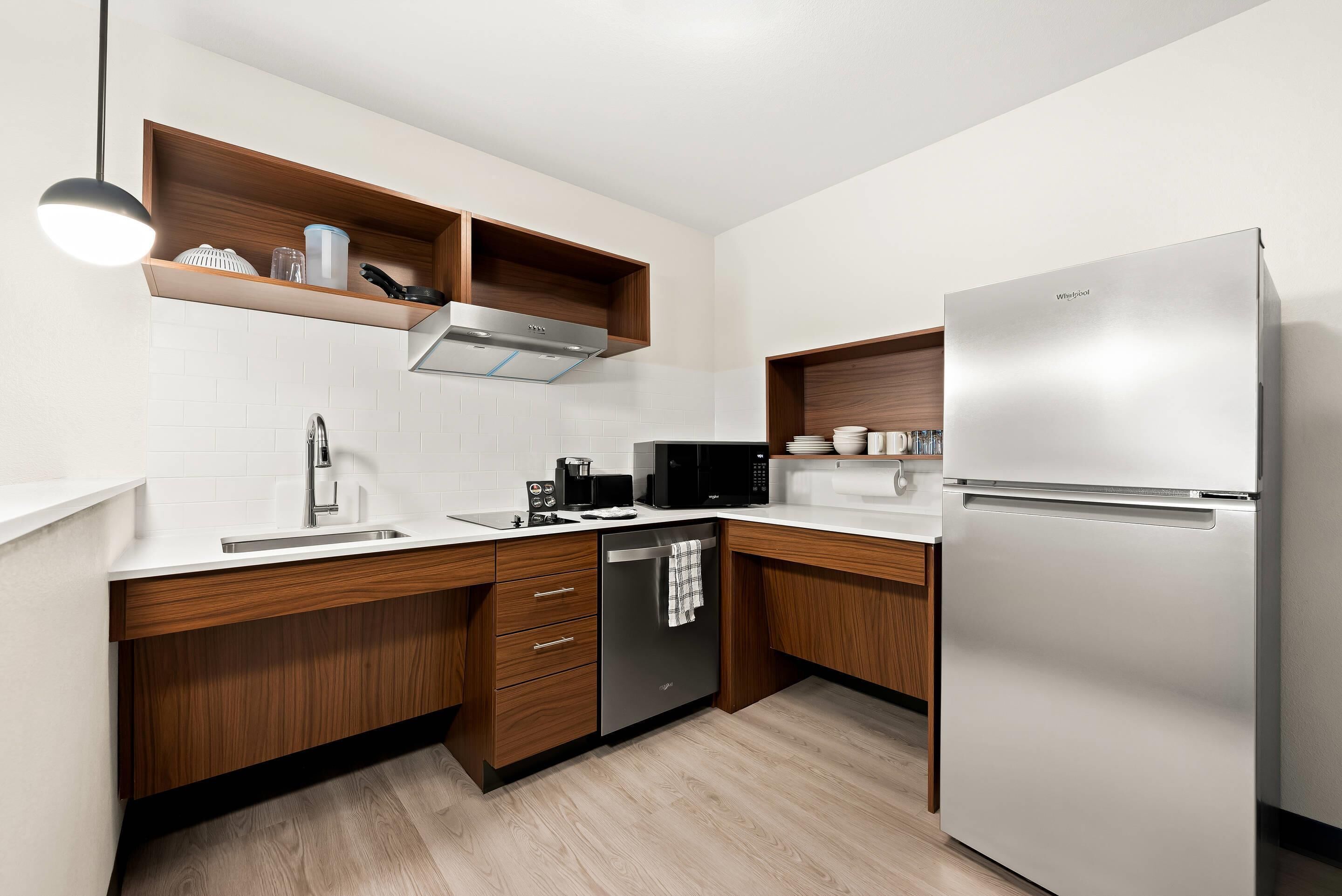 A modern kitchen with a built-in dishwasher, a stainless steel refrigerator, wooden cabinets, and a white tiled backsplash.