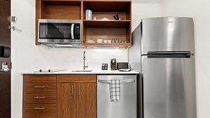 A compact kitchen with a built-in microwave, a stainless steel refrigerator, wooden cabinets, and a dishwasher.