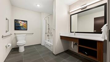 Un baño moderno con inodoro, ducha y lavamanos, equipado con barras de apoyo y un espejo grande.