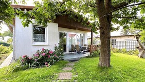 Une maison avec un patio, un coin repas avec des chaises et un jardin fleuri.