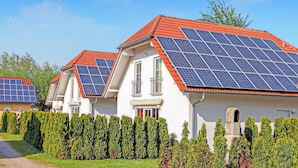 Eine Reihe von Häusern mit Solaranlagen auf den Dächern, ordentlich geschnittenen Hecken und einem klaren Himmel.