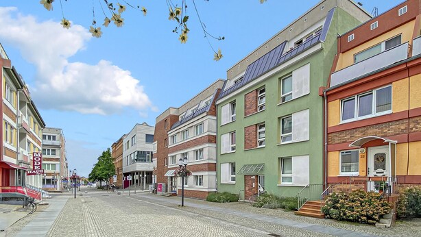 Une rangée d’immeubles résidentiels aux couleurs vives, bordant une rue pavée.