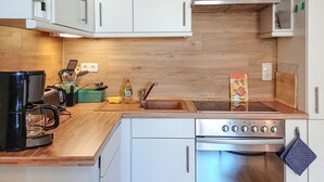 Une cuisine de taille réduite avec des meubles blancs, une cuisinière en acier inoxydable et un plan de travail en bois.