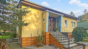 Ein zweistöckiges Haus mit gelber Fassade, rotem Sockel und blauer Tür.