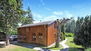 Una baita di legno con tetto spiovente, circondata da alberi e un vialetto fiorito.