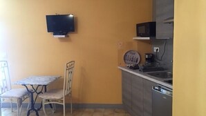 A compact kitchen with a dining table and chairs, a microwave, and a television mounted on the wall. - Studio 3 Personnes Dans Environnement de Charme (Caudrot)