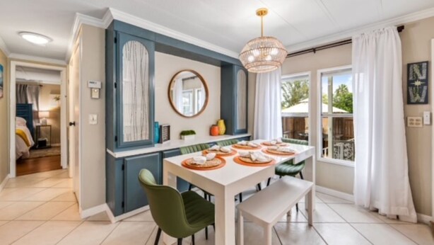 A dining area with a white table set for four, a chandelier, and a view of the outdoors through large windows. - Relaxing 2Bd, 2Ba home in Fort Myers,  close to the beach! Sleeps 6 (Fort Myers)