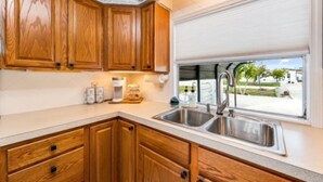 A kitchen with wooden cabinets, a double sink, and a window with a view of the outdoors. - Relaxing 2Bd, 2Ba home in Fort Myers,  close to the beach! Sleeps 6 (Fort Myers)
