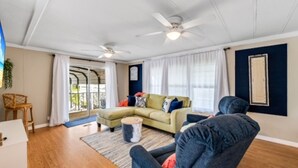 A living room with a sectional sofa, a coffee table, and a ceiling fan. There is a window with curtains and a view of the outdoors. - Relaxing 2Bd, 2Ba home in Fort Myers,  close to the beach! Sleeps 6 (Fort Myers)
