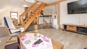 A modern living room with a wooden staircase, a dining area, a kitchen, and a flat-screen TV. - Ferienwohnung Woldegk (Woldegk)