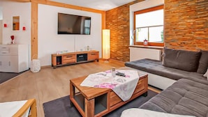 A modern living room with a wooden coffee table, a grey sofa, a TV mounted on the wall, and a window with a view. - Ferienwohnung Woldegk (Woldegk)
