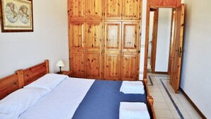 Une chambre avec une armoire en bois, un lit avec du linge de lit blanc et une couvre-lit bleue.