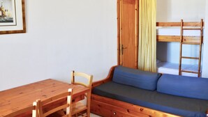 Une pièce de taille modeste, avec une table et des chaises en bois, une banquette intégrée dotée de coussins, une armoire et un lit superposé avec une échelle.