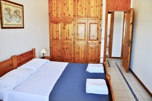 A bedroom with a wooden wardrobe, a bed with white linens, and a blue bedspread.