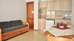 Un espacio habitable compacto con sofá, una mesa de comedor con sillas, una zona de cocina con armarios y un refrigerador, y una puerta de madera.