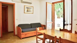 Una habitación con una mesa y sillas de madera, un sofá y un amplio ventanal con cortinas.