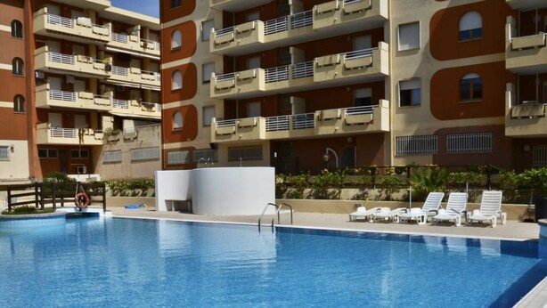 Une piscine équipée d’une bouée de sauvetage, de chaises longues et un bâtiment doté de balcons.