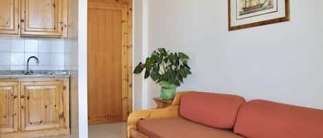 A compact kitchen with wooden cabinets and a sink, a wooden door, a red sofa, and a framed picture on the wall.