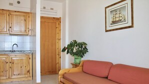 Une cuisine de taille réduite, avec des meubles de rangement en bois et un évier, une porte en bois, un canapé rouge et un tableau encadré accroché au mur.