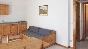 Une pièce comprenant un canapé en bois, une table à manger et un coin cuisine avec des placards en bois.