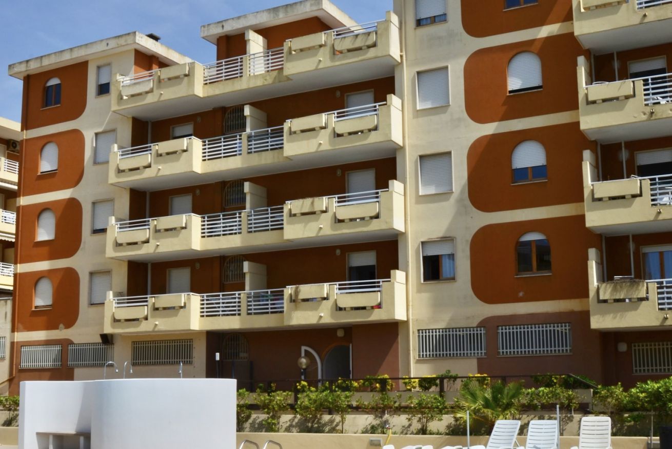A multi-story residential building with balconies, a swimming pool area, and a small garden.