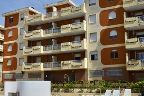 A multi-story residential building with balconies, a swimming pool area, and a small garden.