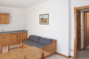 A room with a wooden sofa, a dining table, and a kitchen area with wooden cabinets.