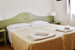 A neatly made bed with white linens, a green headboard, and a patterned bedspread. There are two bedside tables with lamps, and a rolled towel on the bed.