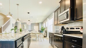A modern kitchen with dark cabinetry, stainless steel appliances, and pendant lighting. - Fun 5BD/5.5BA Home w/Game Room, Pool & Free Resort Access near Disney (Davenport)