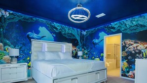 A bedroom with an underwater-themed mural, a bed, bedside tables, and a bathroom visible through an open door. - Fun 5BD/5.5BA Home w/Game Room, Pool & Free Resort Access near Disney (Davenport)