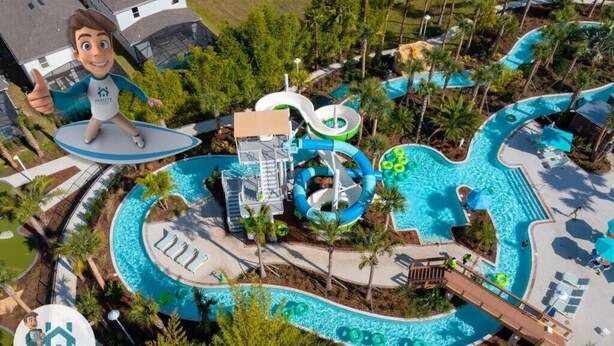 An aerial view of a resort with a large swimming pool, water slides, and palm trees.