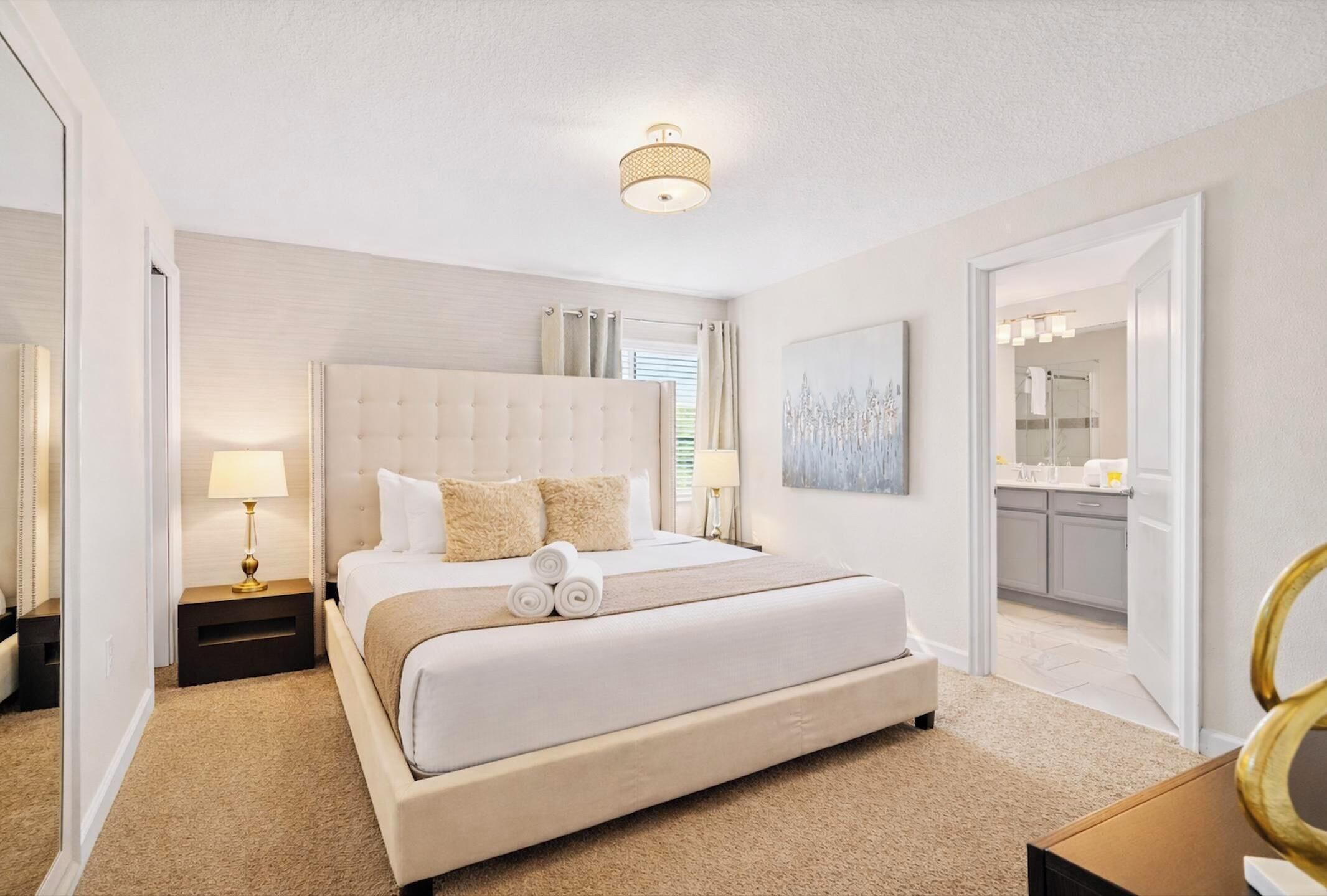 A spacious bedroom with a large bed, a bedside table with a lamp, and a view of the bathroom through an open door.