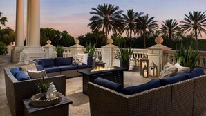 An outdoor seating area with wicker furniture, a fire feature, and palm trees. - High-End 4BD in Luxury Reunion Resort 6mi Disney! (Kissimmee)