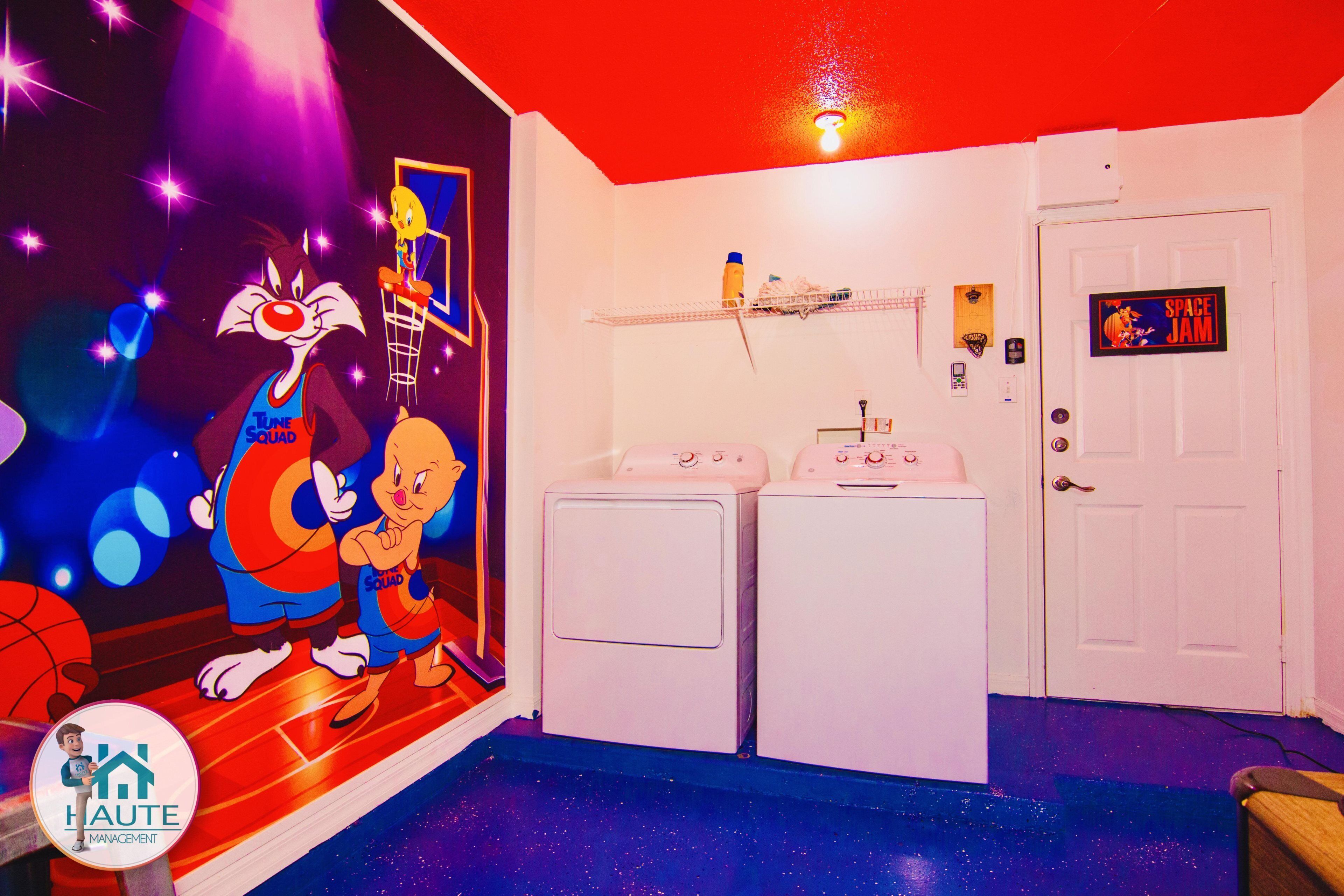 A room with a space-themed mural, two white washing machines, a door labeled "Space Jam," and a small shelf with items.