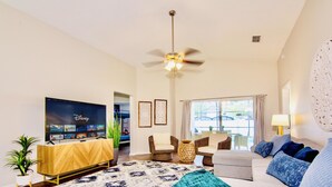 A living room with a flat-screen TV, a ceiling fan, and a large window. - Fantastic 5BD House w/Private Pool - 9mi/Disney! (Clermont)
