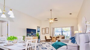 A spacious living room with a dining area, a ceiling fan, and a television displaying Disney content. - Fantastic 5BD House w/Private Pool - 9mi/Disney! (Clermont)