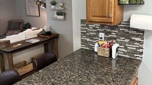 A kitchen with granite countertops, wooden cabinets, a tiled backsplash, and a dining area with a table and chairs.