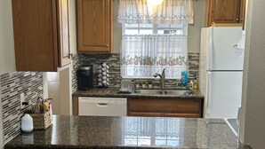 A kitchen with wooden cabinets, a granite countertop, a coffee maker, a sink, and a refrigerator.