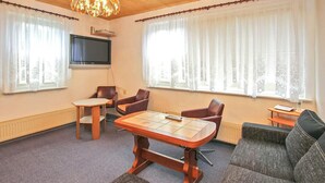 Une chambre d’hôtel avec une table à manger en bois, deux fauteuils en cuir, un canapé et un téléviseur fixé au mur.
