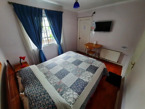 Une pièce comprenant un lit, un bureau, une chaise, un radiateur et un téléviseur fixé au mur.