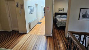A hotel corridor with wooden flooring, a bed with floral bedding, and framed pictures on the walls. - Residencial Metro Republica Santiago (Santiago)