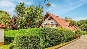Een woonhuis met een rode pannendak, een balkon en een verzorgde haag ervoor.