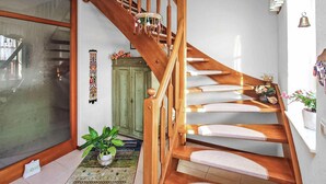 Een houten trap met een leuning, een groene kast, een potplant en een wand met een decoratieve wandhanger.