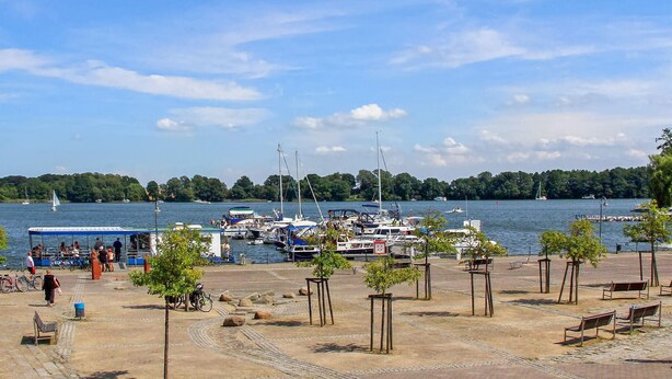Een jachthaven met afgemeerde boten, een zandstrand met bomen en een heldere lucht.