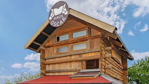 Una baita di legno con un cartello che riporta “HAUS OSCAR” e un tetto rosso.