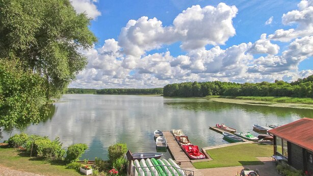 A lakeside view with boats docked, a dock, and a building with a red roof. - Gorgeous apartment in Lychen with sauna (Lychen)