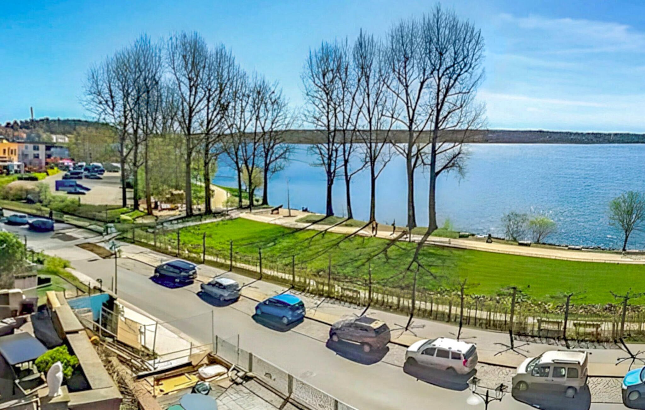 Un parking avec plusieurs voitures, une zone herbeuse et une étendue d’eau en arrière-plan.
