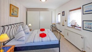 Een slaapkamer met een bed, nachtkastje, lamp, radiator en een raam met gordijnen.