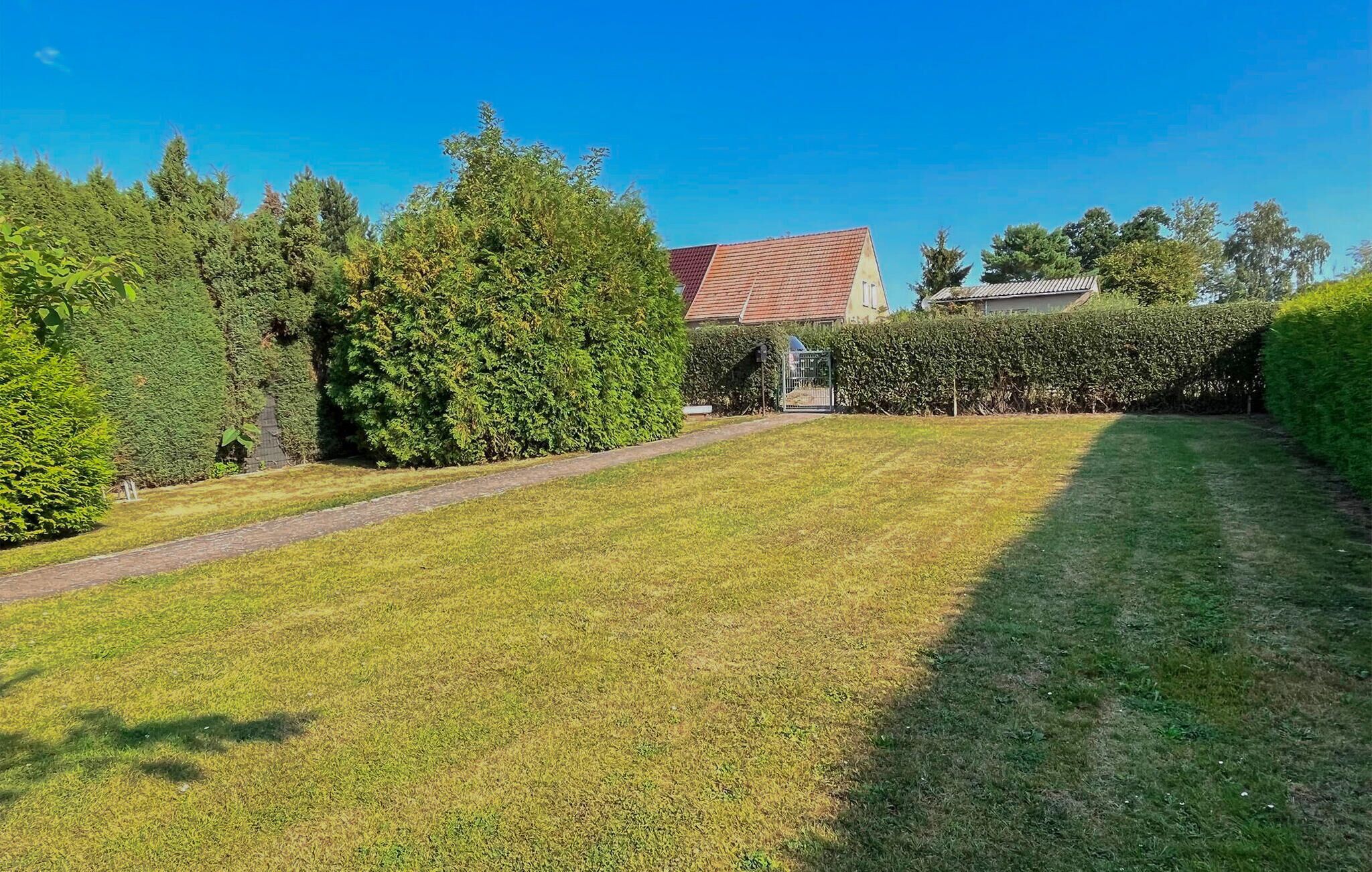 A well-maintained lawn with a paved path, surrounded by neatly trimmed hedges and trees, leading to a building with a red roof.