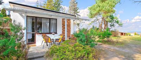 Una casa pequeña con un patio, una mesa con sillas y vistas a los árboles y al cielo circundantes.